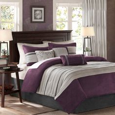 a bed with purple and grey comforters in a bedroom next to two lamps on a table