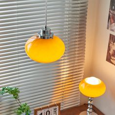 two yellow lights hanging from the ceiling in front of a window with shutters on it