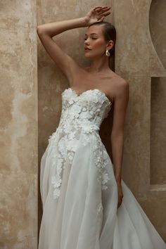 a woman in a wedding dress leaning against a wall with her hand on her head