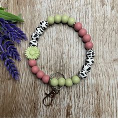 a pink, green and white beaded bracelet on a wooden table next to purple flowers