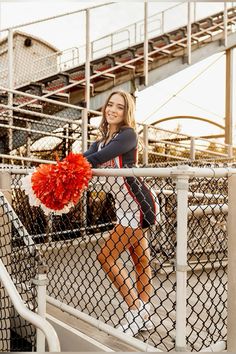 a woman holding a red pom - pom in front of a metal fence