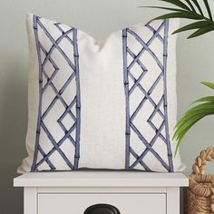 a white and blue pillow sitting on top of a table next to a potted plant