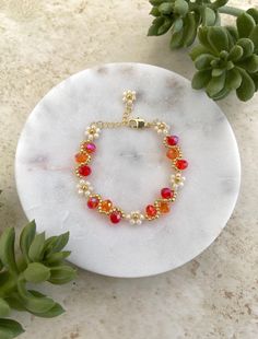 a bracelet with red and yellow beads sits on a marble plate next to green plants