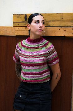 a woman standing in front of a wooden wall wearing a colorful sweater and black shorts