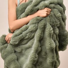 a woman is wrapped in a large green fur coat with one hand on her hip