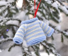 a knitted mitt ornament hanging from a christmas tree in the snow