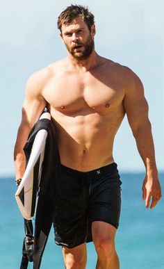 a shirtless man holding a surfboard on the beach