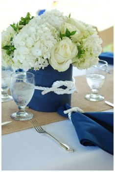 the table is set with white flowers in a blue vase and silverware on it