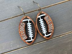 two wooden earrings with footballs on them sitting on top of a wooden table next to each other