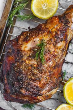 a piece of meat sitting on top of a metal rack next to lemons and rosemary