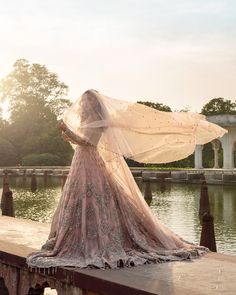 a woman in a wedding dress is standing on a bridge with her veil blowing in the wind