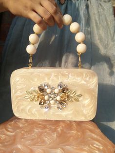 💥 Detailed Description: Elevate your accessory game with our trendy resin clutch bag, featuring an exquisite beaded handle and stunning pearl diamond embellishments. This handcrafted piece is perfect for making a bold statement at weddings, parties, and special occasions. Each clutch is meticulously crafted with high-quality resin and adorned with intricate beadwork and faux pearls, ensuring a unique and luxurious accessory. 💥 Product Details ● Handmade item ● Materials: High-quality Resin, Be White Portable Box Bag For Gift, White Clutch With Detachable Handle For Party, White Evening Bag With Detachable Handle For Events, Elegant White Box Bag For Gift, Elegant Cream Box Bag For Formal Occasions, Luxury White Evening Bag As Gift, Cream Rectangular Evening Box Bag, Cream Rectangular Box Bag For Evening, Formal White Clutch Box Bag