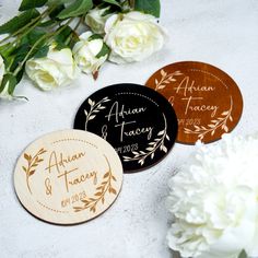 three wooden coasters with names and date printed on them next to white flowers in the background