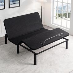 a black futon bed frame sitting on top of a white rug in front of a window