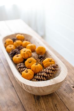 a wooden bowl filled with pine cones and pumpkins