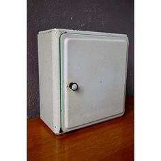 an old fashioned white refrigerator sitting on top of a wooden table next to a gray wall