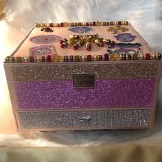 a pink and purple box with lots of jewelry on it sitting on a white furnishing