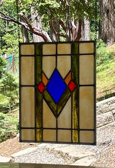 a stained glass window hanging from the side of a tree in front of some trees