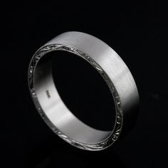 a silver ring with intricate engraving on the outside and inside, against a black background