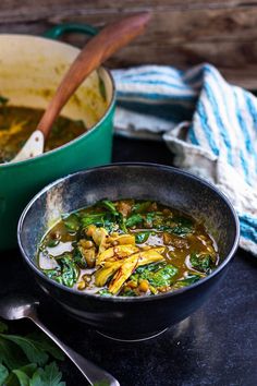 a bowl filled with soup next to a pot full of stew and a wooden spoon