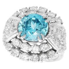 A stunning vintage 5.70 Carat high zircon and 3.15 Carat diamond, 18k white gold dress ring; part of our diverse vintage jewelry and estate jewelry collections. This stunning, fine and impressive blue zircon ring has been crafted in 18k white gold. The pierced decorated, cluster style setting is ornamented with a 2.82Ct Old European round cut blue zircon, four swallow-tip claw set in relief to the center of the design. The zircon is encircled by twenty individually three claw set eight-cut diamo Blue Zircon Ring, Vintage Cluster Ring, White Gold Dress, Unique Diamond Engagement Rings, Branch Ring, Gold Cocktail Ring, Gold Cocktail, Vestidos Vintage, Zircon Ring