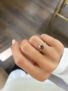 a woman's hand holding a ring with a brown diamond in it on top of a wooden floor