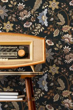 an old radio sitting on top of a wooden stand next to a floral wallpaper