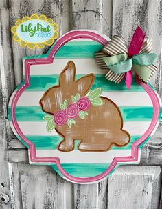 a wooden sign with a bunny painted on it's side and a bow hanging from the front