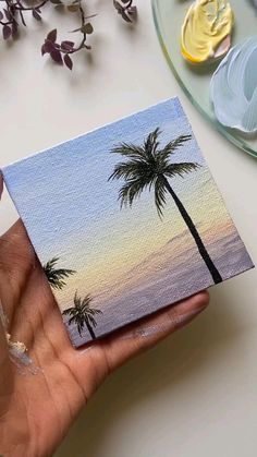 a person holding up a small piece of paper with palm trees painted on the side