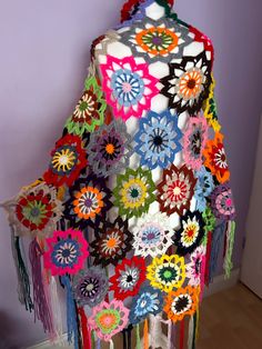 a multicolored crocheted shawl hanging from a hook on a wall