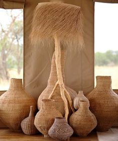 several vases are arranged on the floor in front of a window with an animal's tail sticking out of it