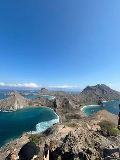 two people taking pictures on top of a mountain overlooking the ocean and mountains in the distance