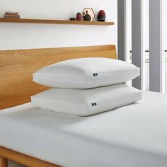 two pillows stacked on top of each other on a bed with white sheets and wooden headboard