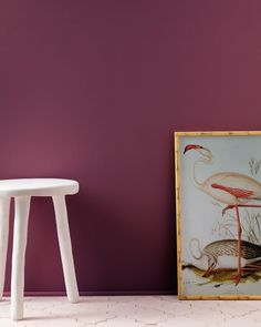 a white stool sitting next to a painting on a wall near a table and chair