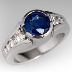 This delightful ring is centered with one (1) round mixed cut natural sapphire set into a half-bezel setting. The top face of the shank is accented with four (4), channel set, round brilliant cut diamonds. The ring measures 9.4mm at the top, rises 7.1mm above the finger, tapering to 3.4mm wide and 1.6mm thick at the base of the shank. This ring is currently a size 6.5. The sapphire shows light abrasions. Blue Diamond Platinum Ring With Polished Finish, Blue Platinum Diamond Ring With Polished Finish, Modern Sapphire Ring With Bezel Setting For Formal Events, Blue Diamond Channel Set Ring, Blue Diamond Ring Channel Set, Blue Diamond Ring With Channel Set, Blue Diamond Ring With Channel Setting, Modern Sapphire Ring In Platinum With Brilliant Cut, Modern Platinum Sapphire Ring With Brilliant Cut