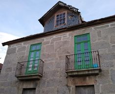 two windows with green shutters on the side of an old stone building in europe