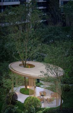 a circular wooden structure in the middle of trees and bushes, with benches around it