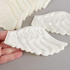 two white angel wings sitting on top of a table next to someone's hand