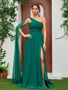 a woman standing in front of a door wearing a green dress with one side slit