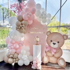 a teddy bear sitting next to a cake and balloons