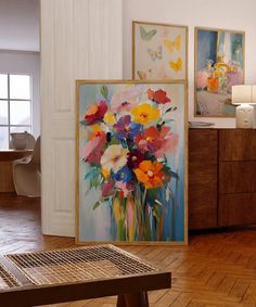 paintings on the wall in a room with wooden flooring and wood furniture, along with a coffee table