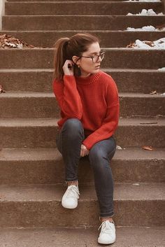 a woman sitting on the steps talking on her cell phone while wearing glasses and a red sweater