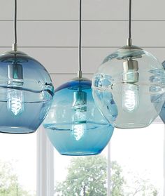 three blue and clear glass globes hanging from a ceiling in front of a window