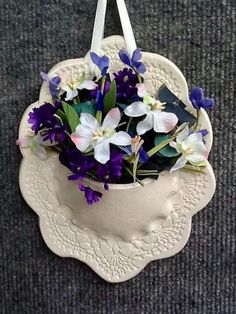 purple and white flowers are in a hanging planter on a gray carpeted surface