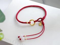 a red string bracelet with two charms and a gold plated charm on it's end