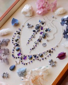 an assortment of jewelry is displayed in a box with flowers on the table next to it