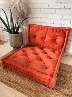 an orange chair sitting on top of a rug next to a potted plant