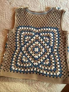 a crocheted sweater sitting on top of a bed next to a quilted blanket