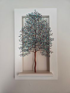 a small tree with blue leaves in a white frame on the wall above a shelf