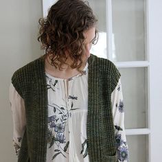 a woman standing in front of a window wearing a green sweater and white shirt with flowers on it